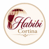A circular logo or label with the words 'Habibi Cortina' in elegant typography, featuring a red and gold curtain illustration on a cream background.